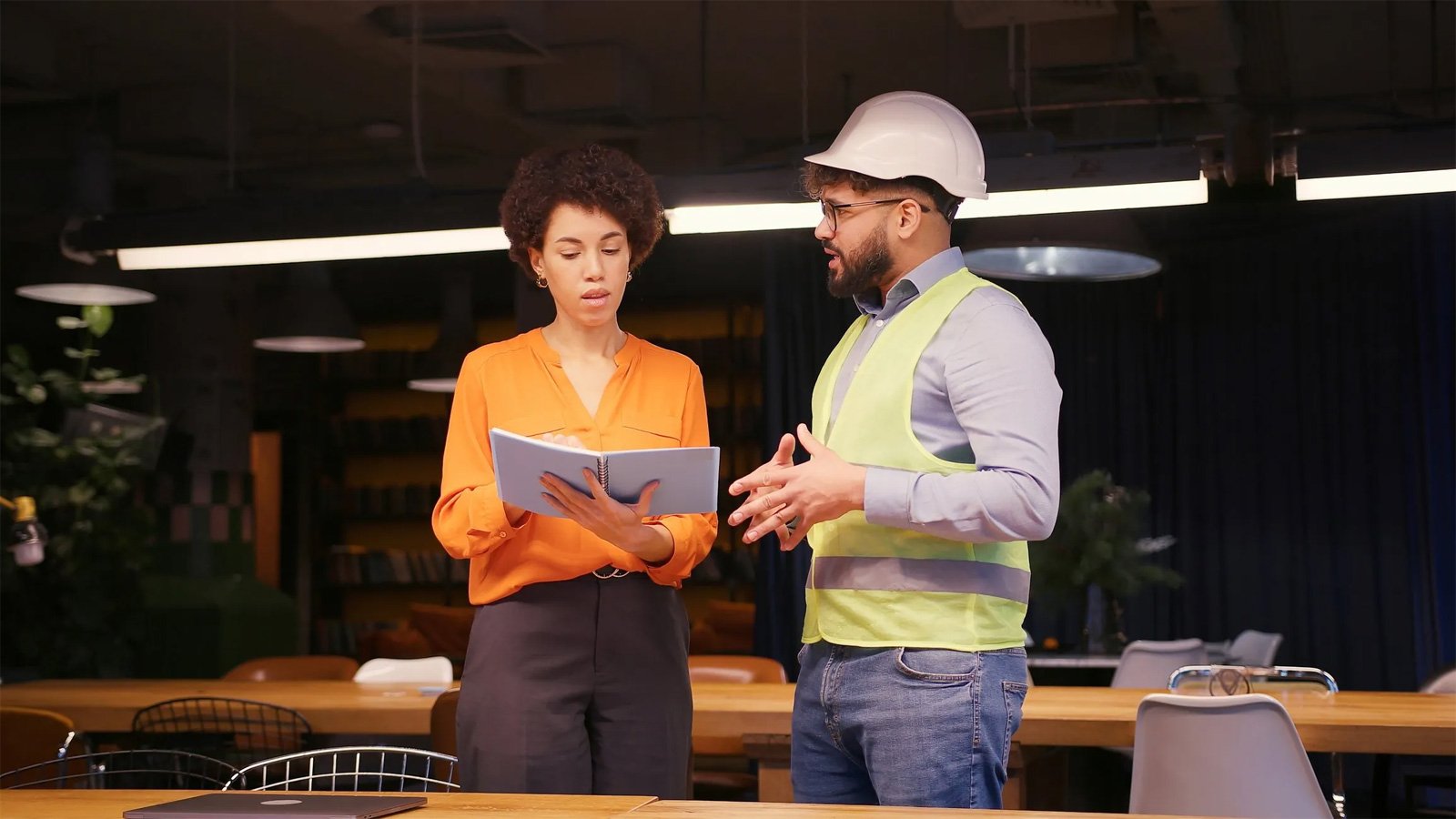Male project manager discussing building plan with female engineer in hard hat and safety vest, concluding their successful meeting, handshake in modern office. Deal concept